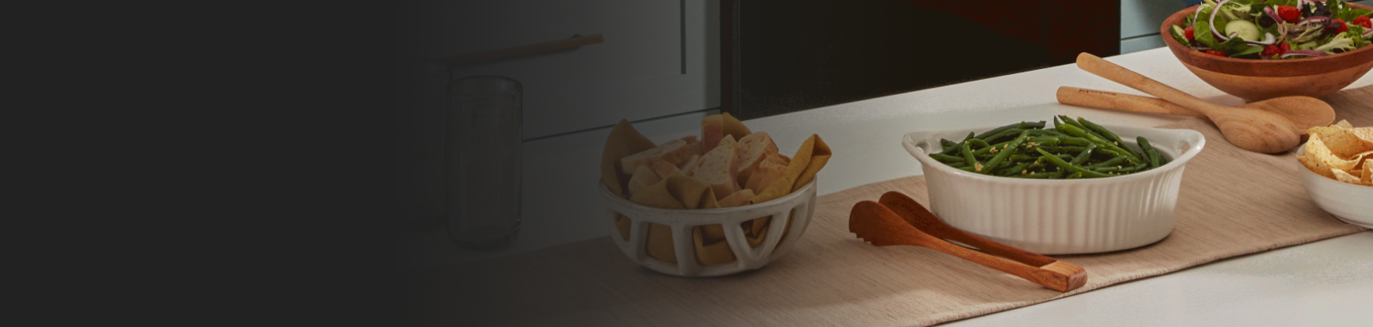 Ceramic pot of cooked green beans next to salads and breads