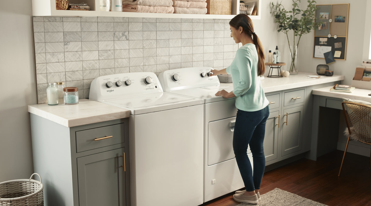 A woman using a Whirlpool® dryer next to a matching washer A woman using a Whirlpool® dryer next to a matching washer