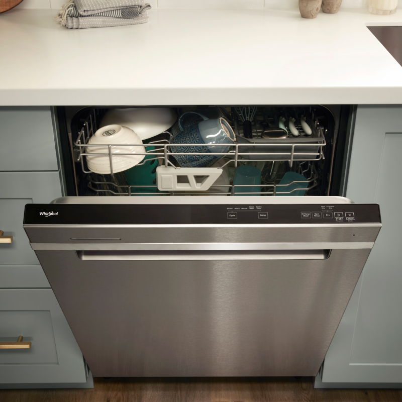 A partially opened Whirlpool® dishwasher with dishes inside.