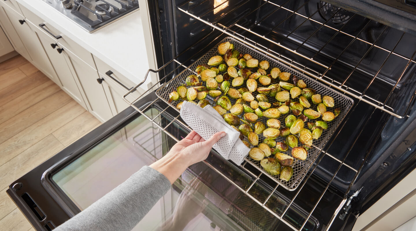A person removing a tray of Brussels sprouts from an oven A person removing a tray of Brussels sprouts from an oven