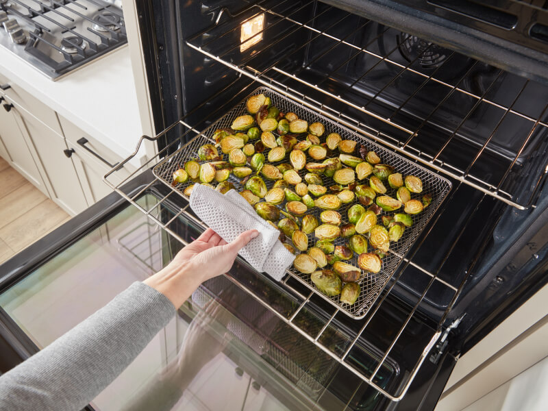 A person removing a tray of Brussels sprouts from an oven A person removing a tray of Brussels sprouts from an oven