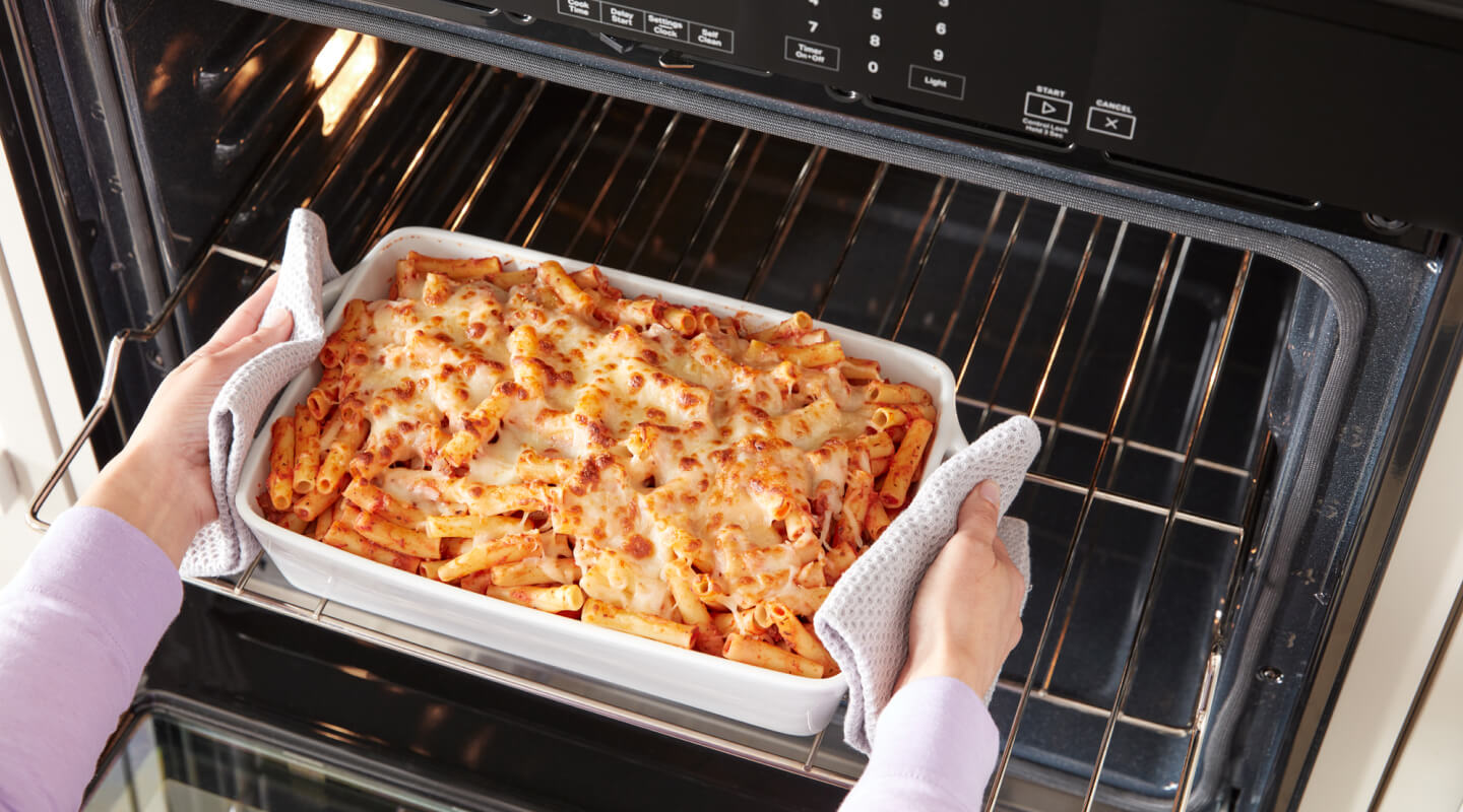 A person removing a dish of baked ziti from an oven A person removing a dish of baked ziti from an oven