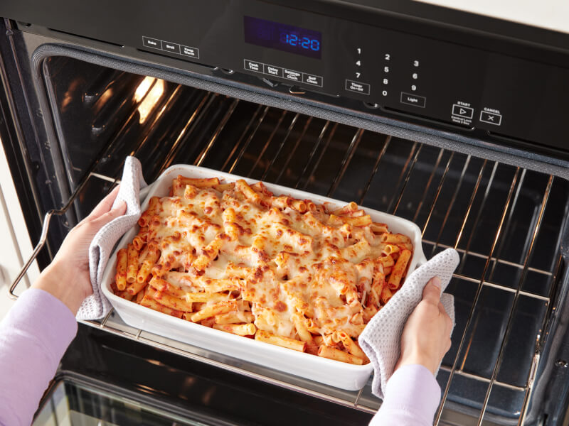 A person removing a dish of baked ziti from an oven A person removing a dish of baked ziti from an oven