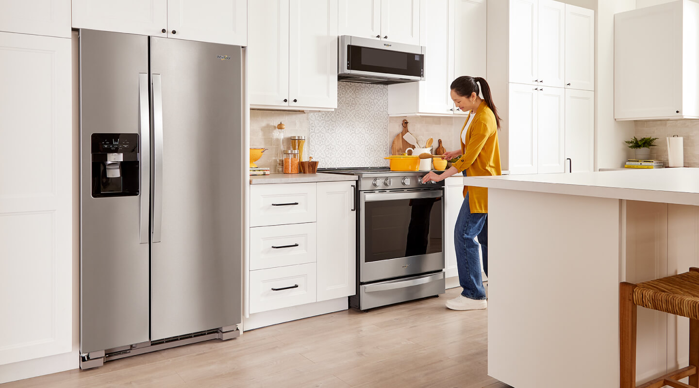 A person cooking in a kitchen near a stainless steel side-by-side refrigerator