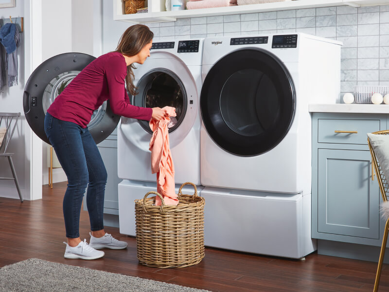Person transferring laundry from a wicker basket into a white front load washer Person transferring laundry from a wicker basket into a white front load washer