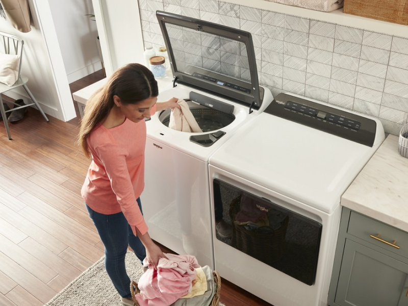Person loading clothing into white top-load washer