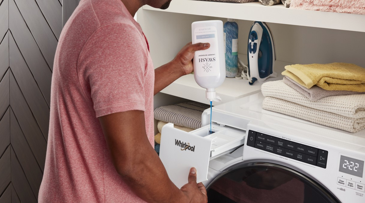 Person filling washing machine with Swash laundry detergent.