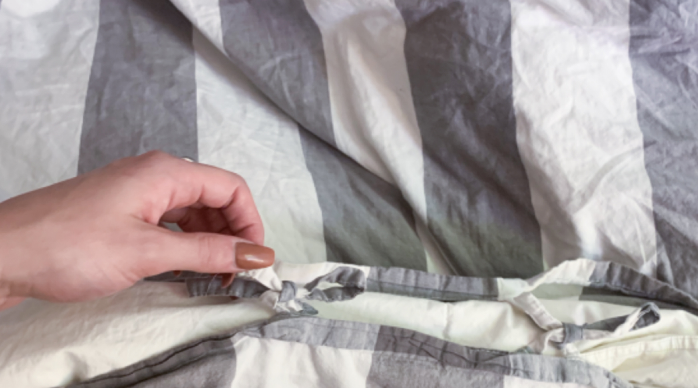 Person removing gray and white striped duvet cover from comforter