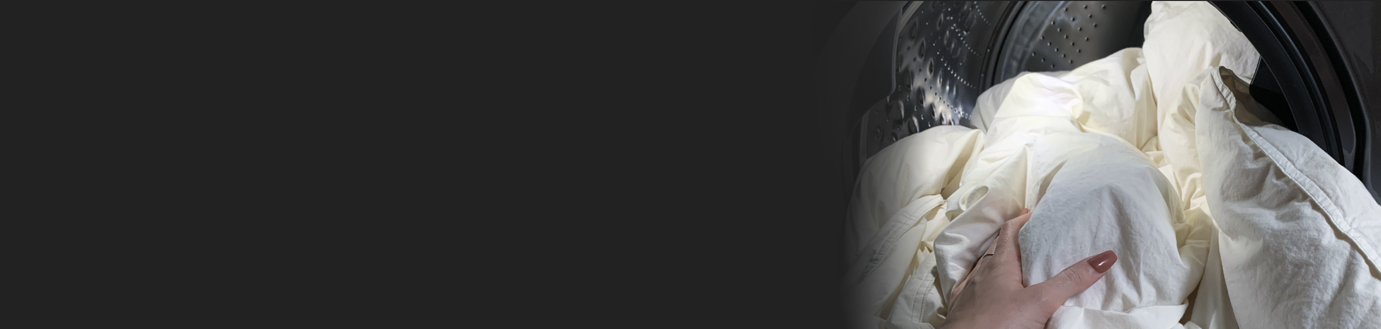 Hand touching white comforter inside dryer drum.