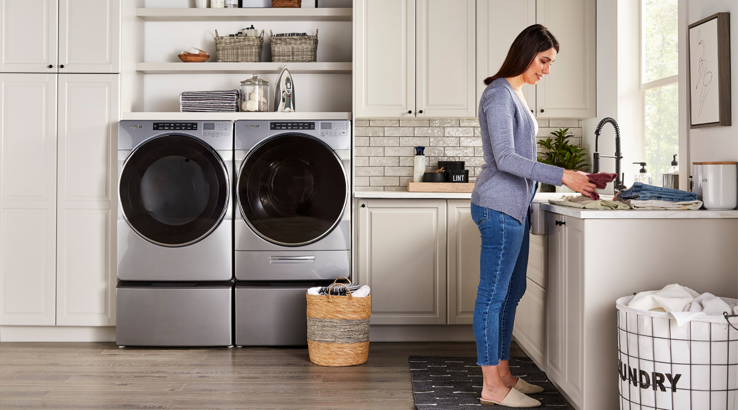 Woman in a laundry room with stainless steel Whirlpool® front load washer and dryer set Woman in a laundry room with stainless steel Whirlpool® front load washer and dryer set
