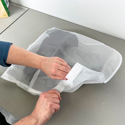 A person putting laundry in a mesh laundry bag