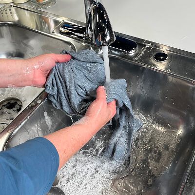 A person rinsing leggings under a faucet in a sink