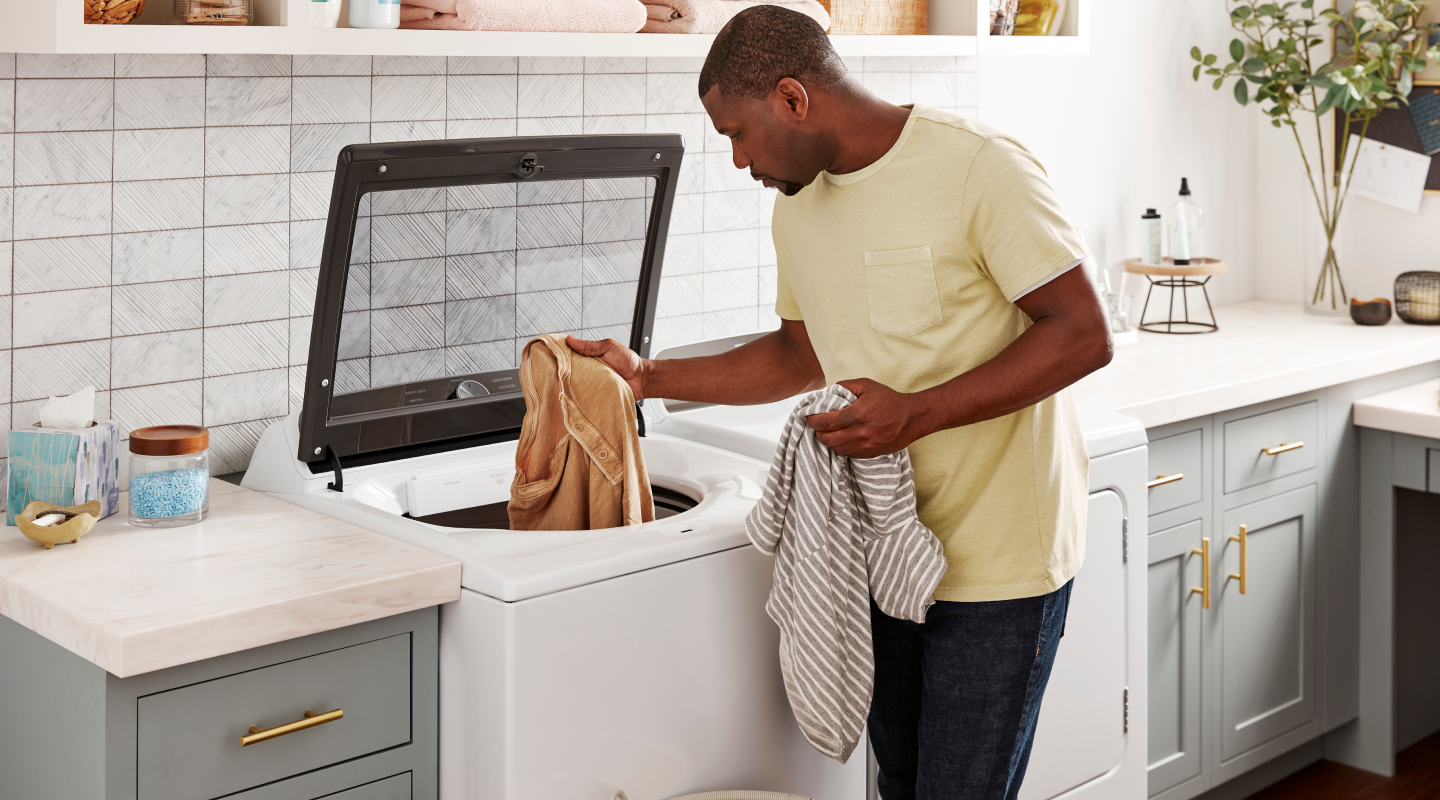 A man loading a top-load washer with clothes A man loading a top-load washer with clothes