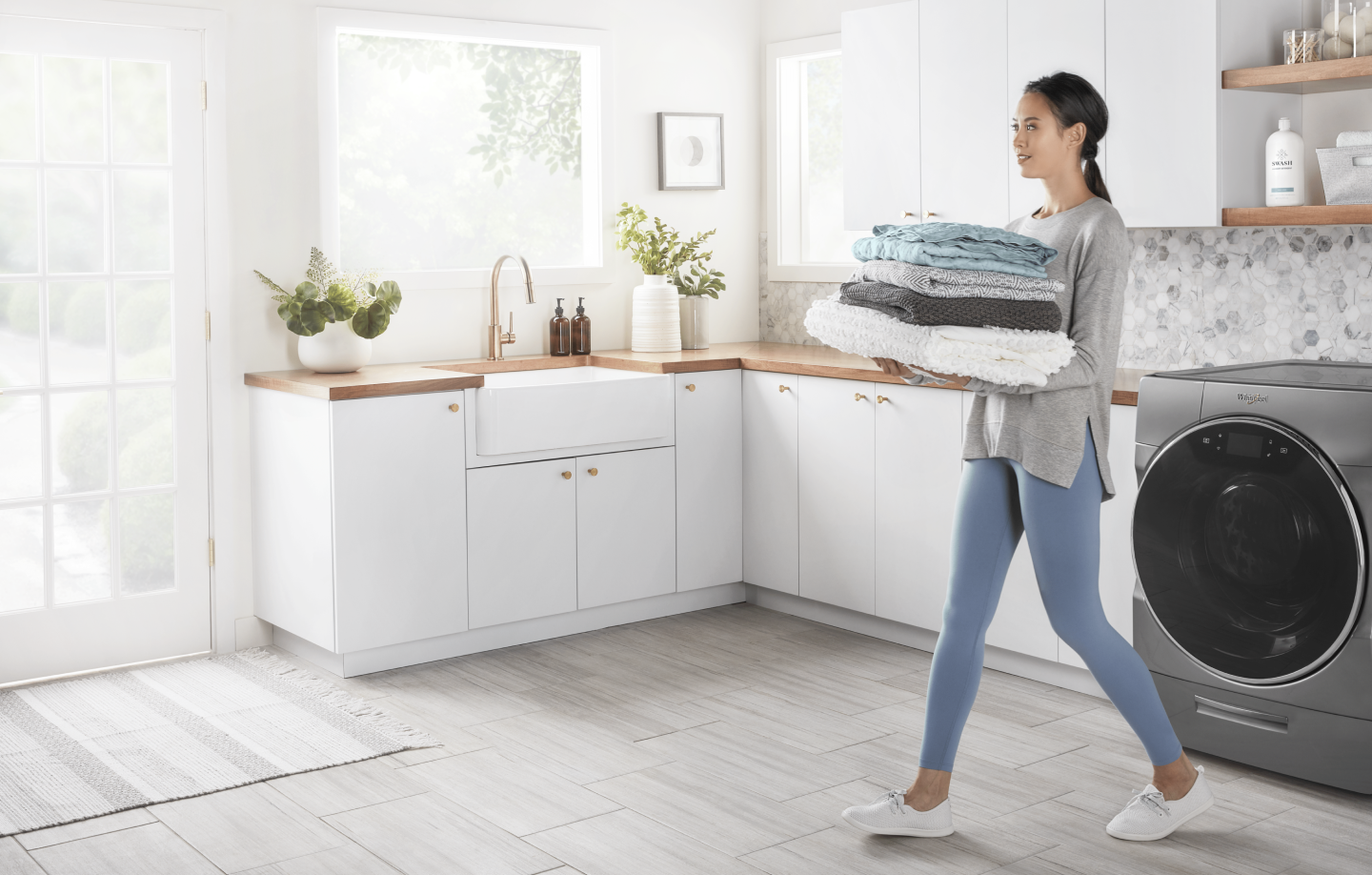 A woman carrying folded laundry cleaned by a Whirlpool® washing machine A woman carrying folded laundry cleaned by a Whirlpool® washing machine