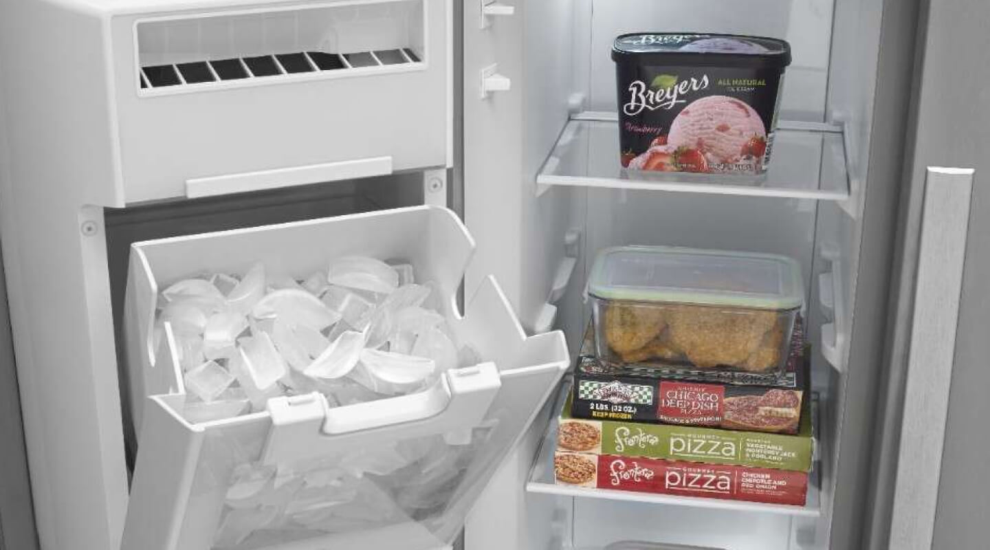 Open freezer door in side-by-side refrigerator revealing open, in-door ice maker