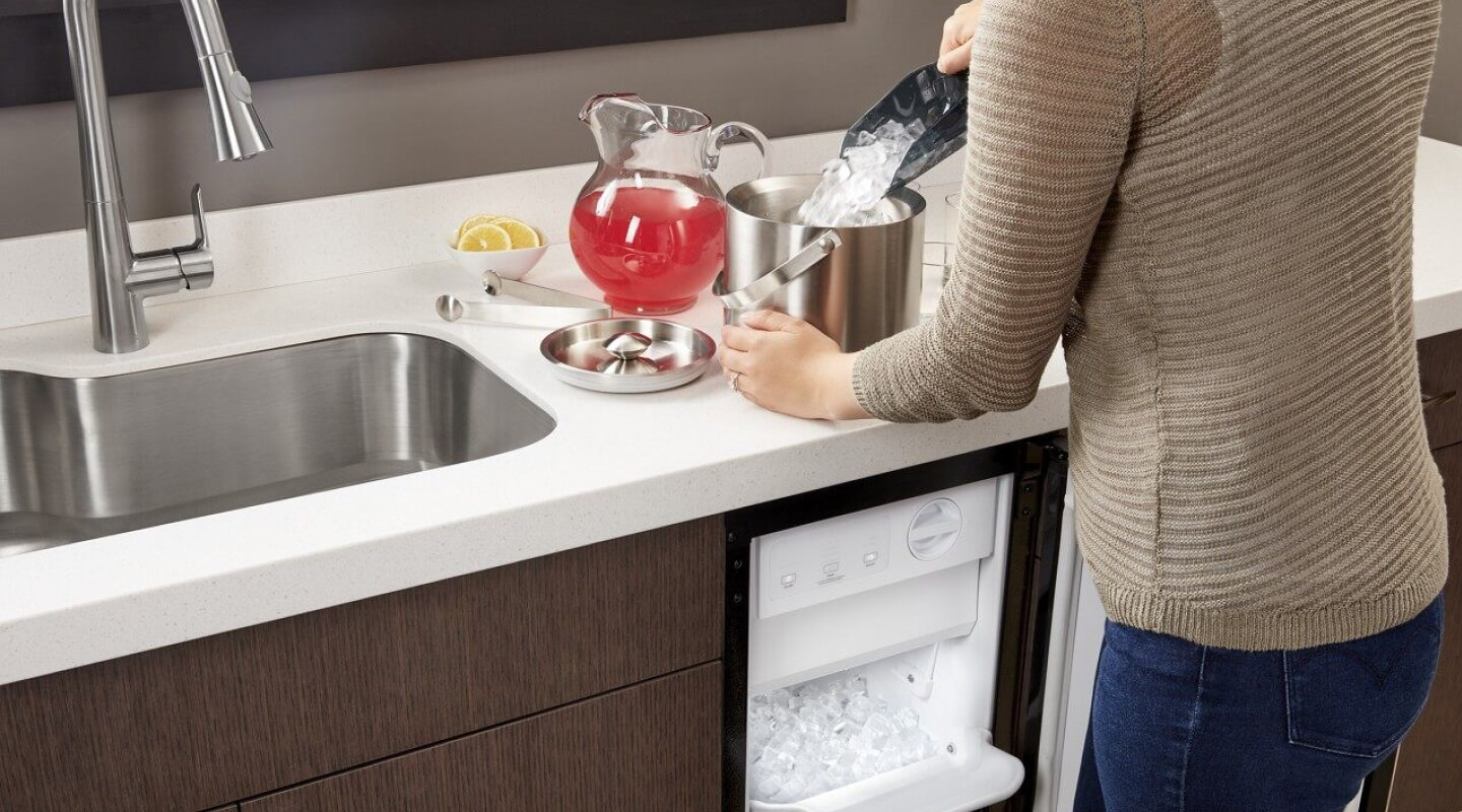 Woman scooping ice out of ice maker and into ice bucket on counter