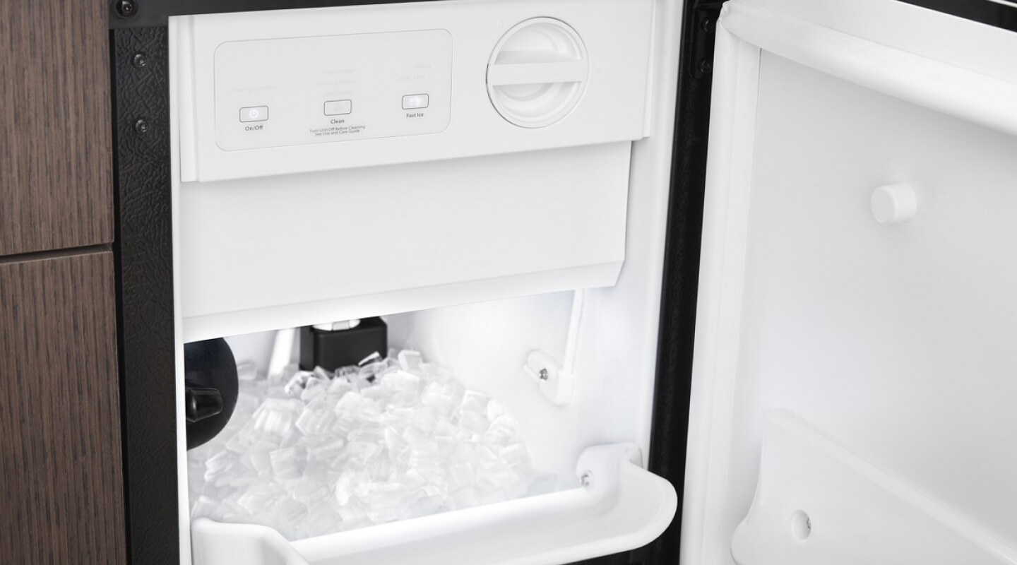 Close-up of open, standalone ice maker installed in brown cabinetry