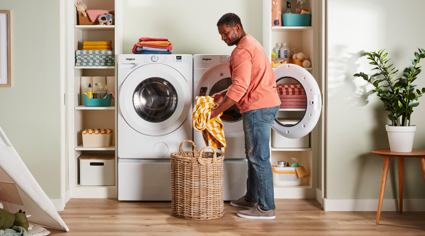 Person placing clothes in laundry basket in front of Whirlpool® Washer and Dryer