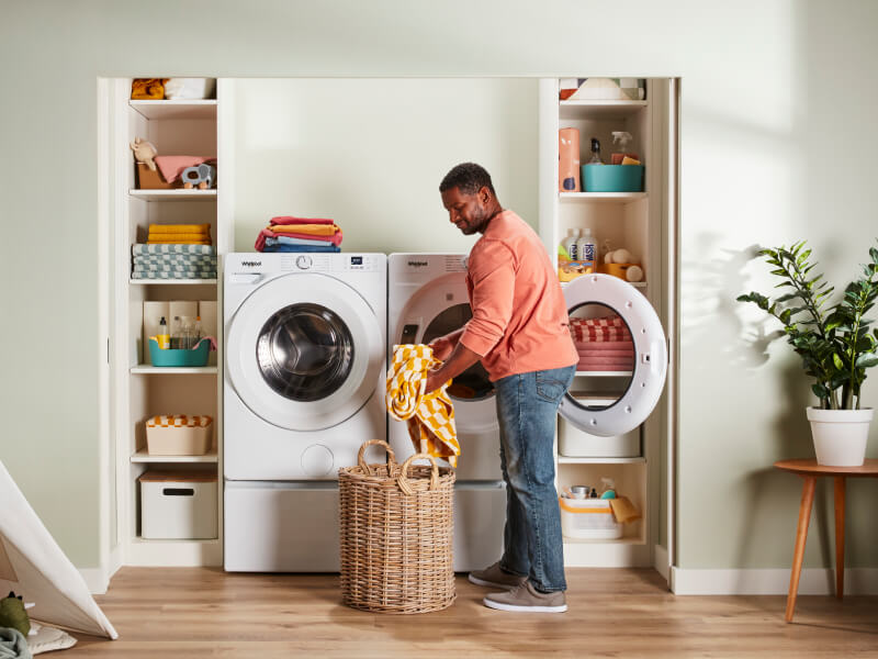 Person placing clothes in laundry basket in front of Whirlpool® Washer and Dryer