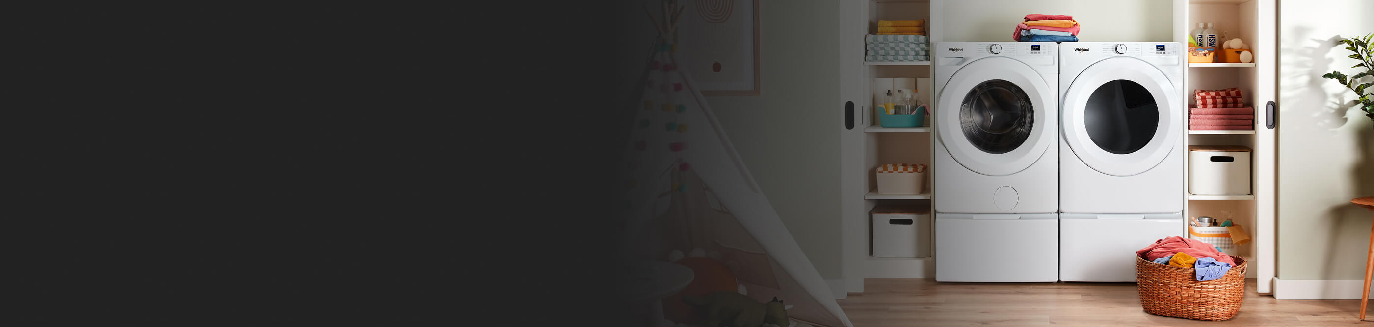 A white Whirlpool® Front Load Washer and Dryer on top of pedestals and inside a wide laundry closet with shelves on each side