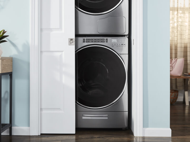 Stackable washer and dryer in a closet with door slightly ajar Stackable washer and dryer in a closet with door slightly ajar