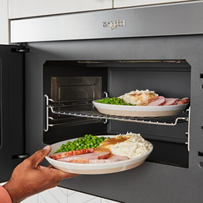 Person loading multiple dishes into and under cooking rack in microwave