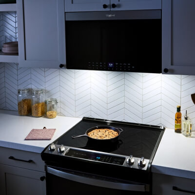 Lighting on over-the-range microwave illuminating a dish cooking on stovetop