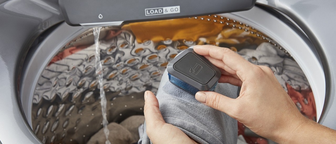 A person using a scrub brush filled with detergent on a stained piece of clothing A person using a scrub brush filled with detergent on a stained piece of clothing