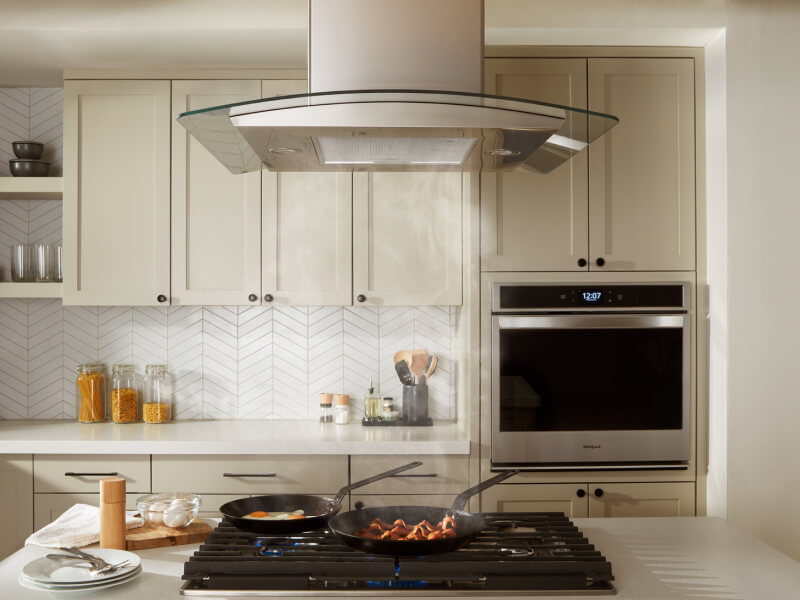Bacon and eggs simmering on a gas cooktop underneath an island canopy hood Bacon and eggs simmering on a gas cooktop underneath an island canopy hood