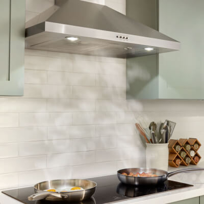 Stainless steel range hood over two pans cooking on a cooktop