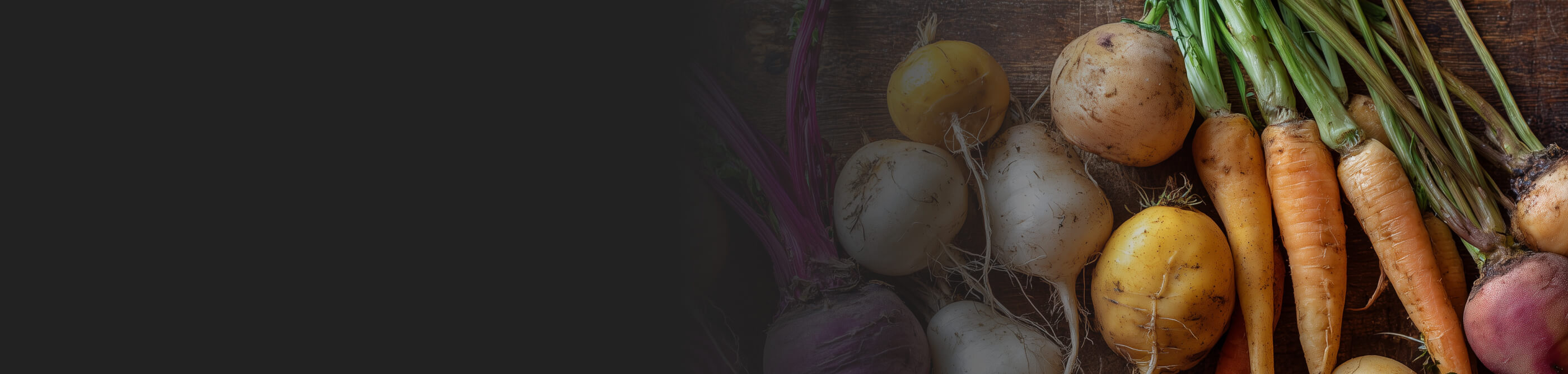 A selection of root vegetables, including carrots, on a wood background