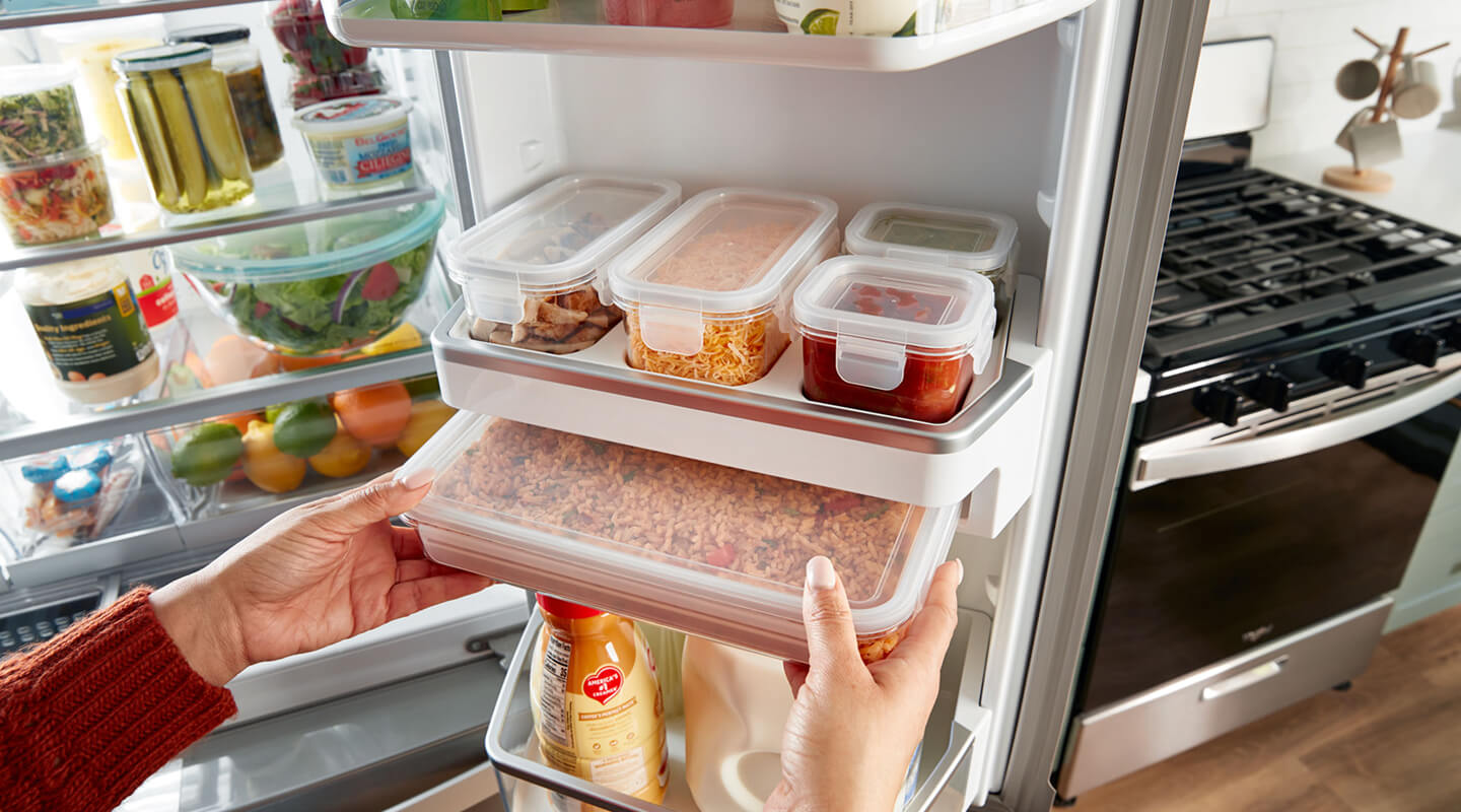 A person placing food stored in containers in a refrigerator 