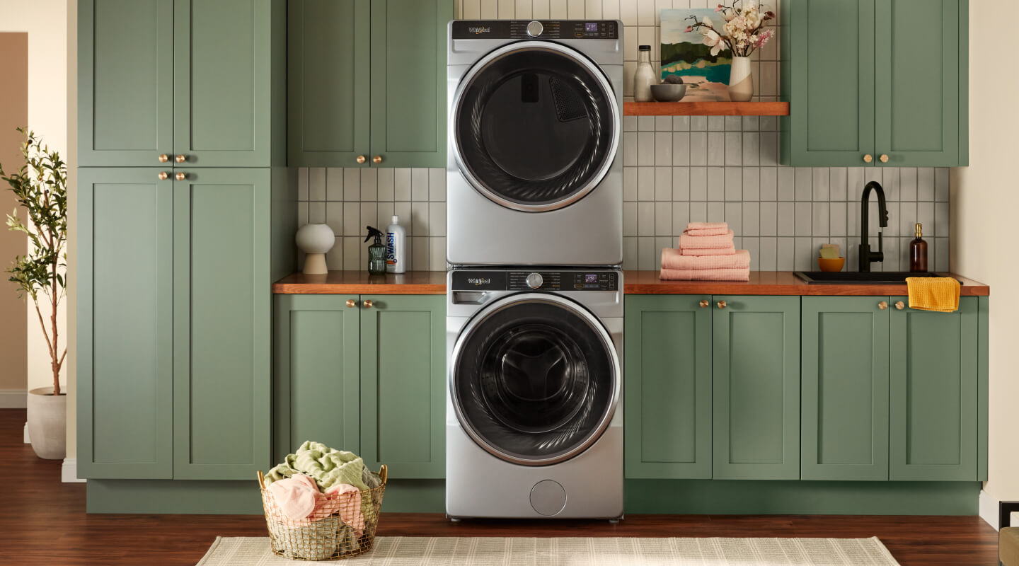 Stacked front load washer and dryer surrounded by green cabinets Stacked front load washer and dryer surrounded by green cabinets