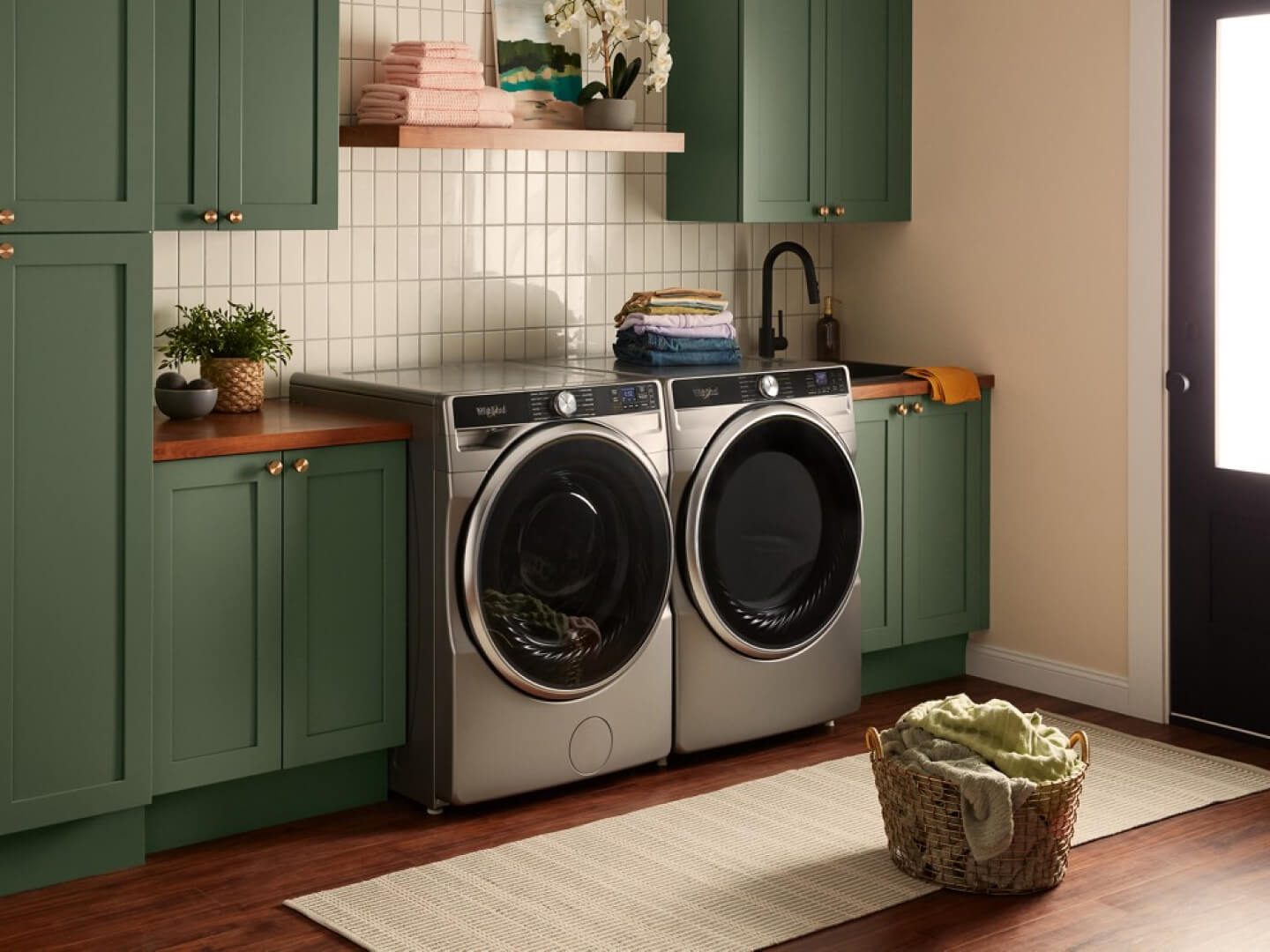 A front load laundry pair in a laundry room with green cabinetry