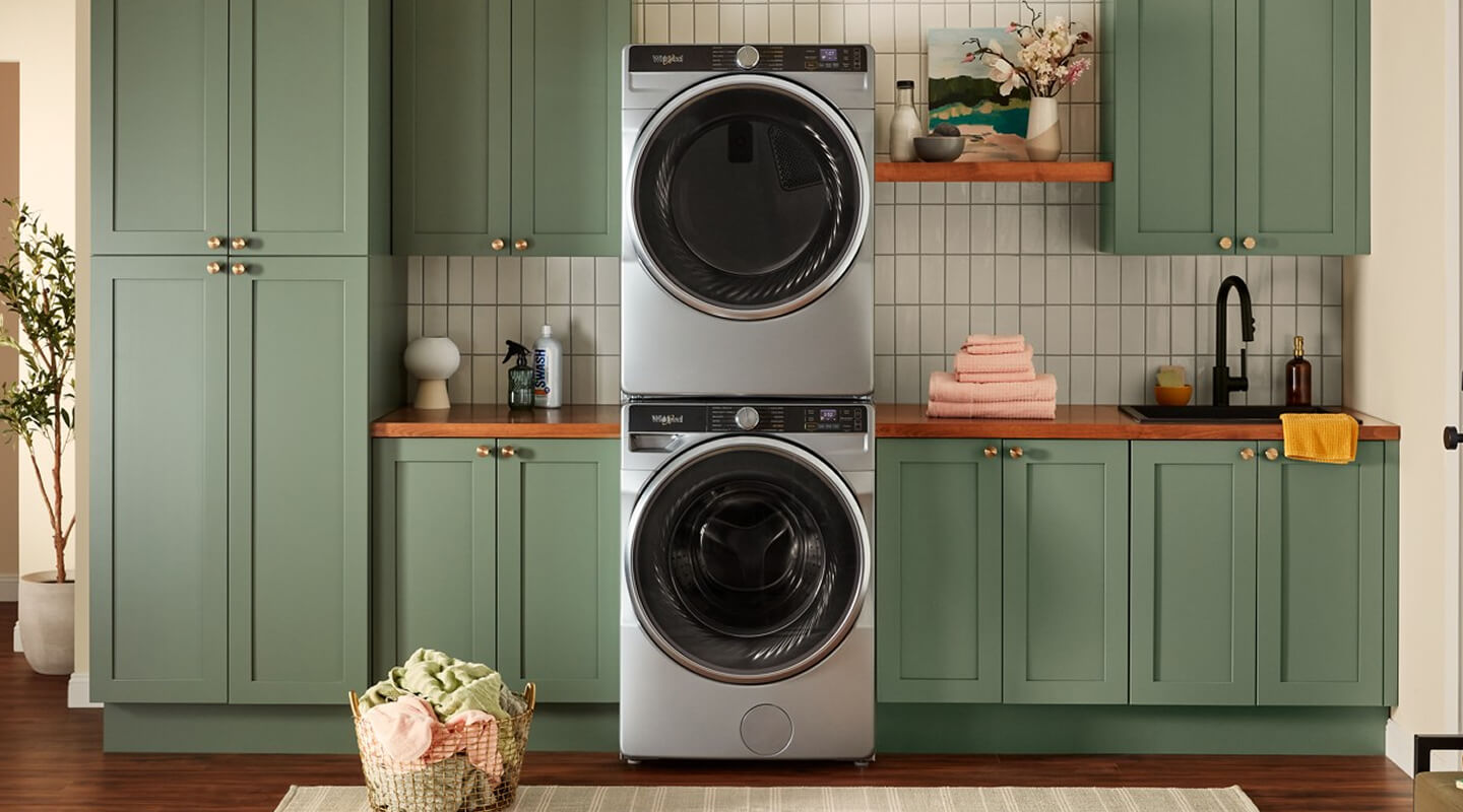 Stainless steel front load washer and dryer in a laundry room with green cabinetry