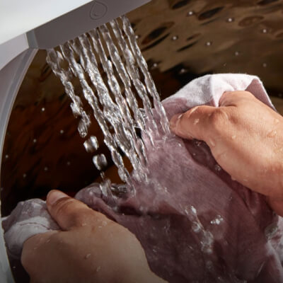 Close up of the interior of a Whirlpool® Washer filling with water as a person pretreats clothing odor