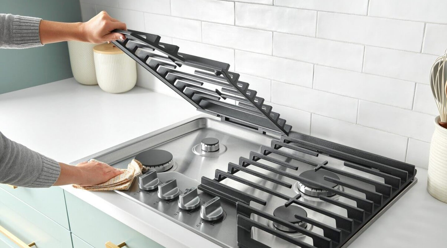 Person lifting the grate on a gas cooktop Person lifting the grate on a gas cooktop