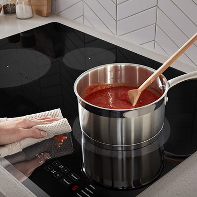 Person wiping spaghetti sauce splatter from ceramic glass cooktop surface