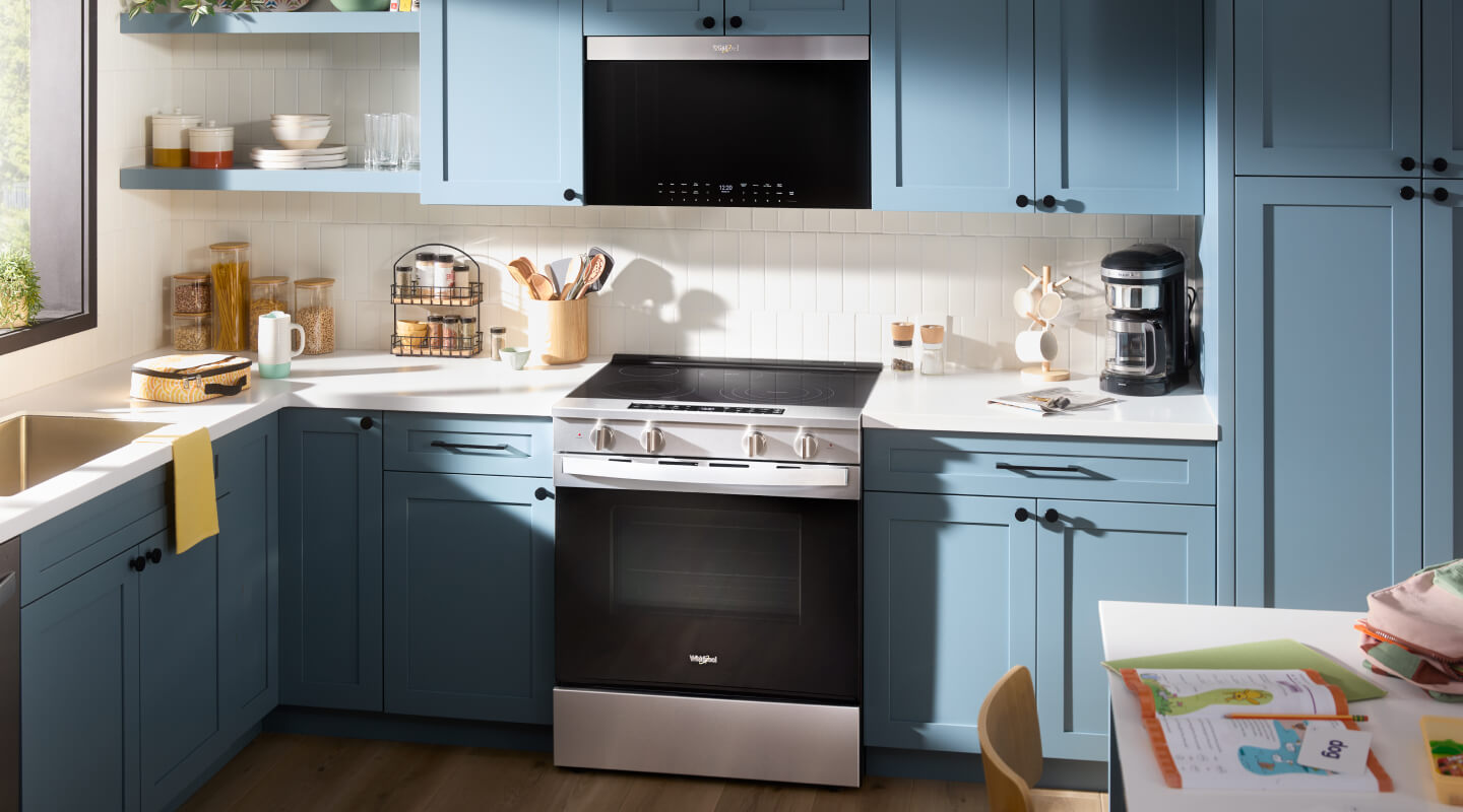 An over-the-range microwave above an electric slide-in range inside a kitchen with blue cabinets