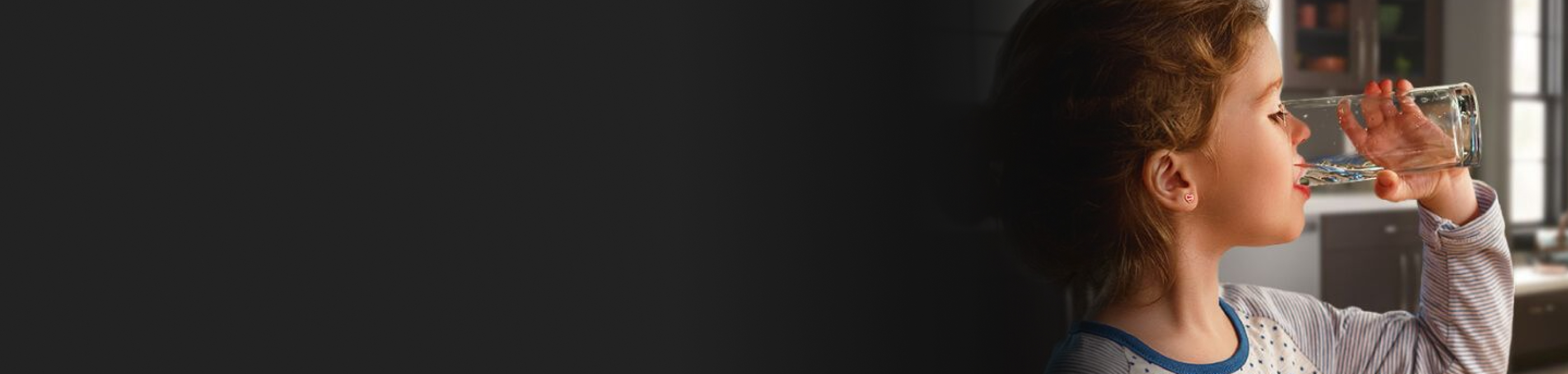 A young girl drinking out of a glass of water