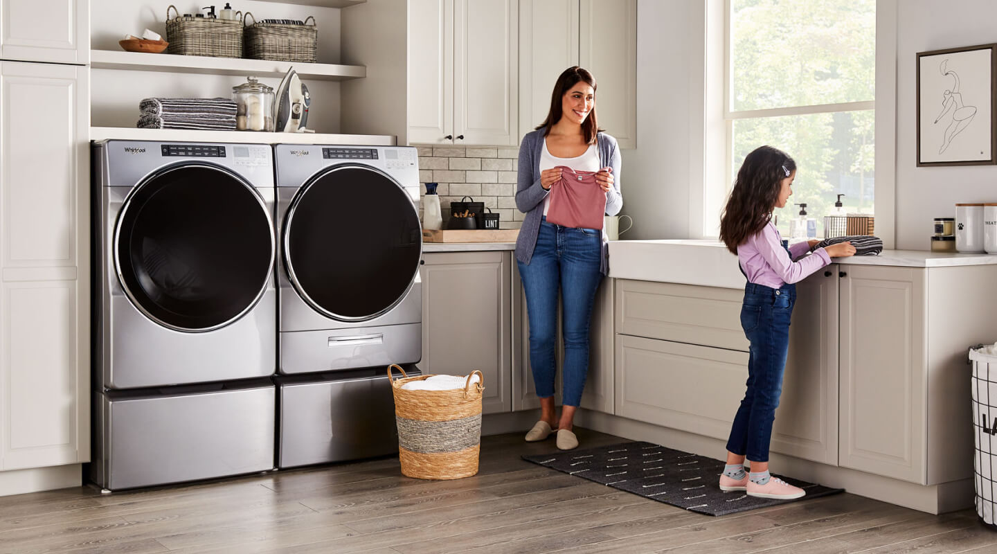 A parent and child in a laundry room with a Whirlpool® Front-Load Washer and Dryer set A parent and child in a laundry room with a Whirlpool® Front-Load Washer and Dryer set