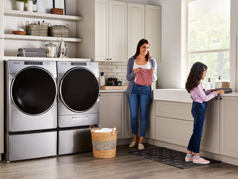 A parent and child in a laundry room with a Whirlpool® Front-Load Washer and Dryer set A parent and child in a laundry room with a Whirlpool® Front-Load Washer and Dryer set