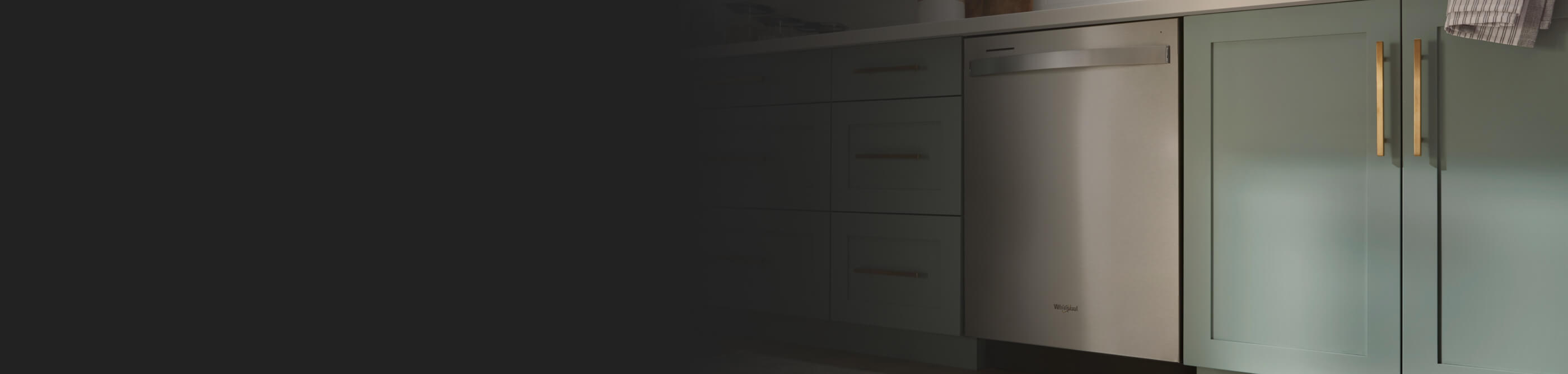 A Whirlpool® Built-In Dishwasher with Top Control and a towel handle placed between green cabinets and under white countertops