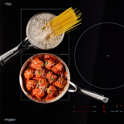 An overhead view of pasta and meatballs cooking on two separate burners of an induction cooktop