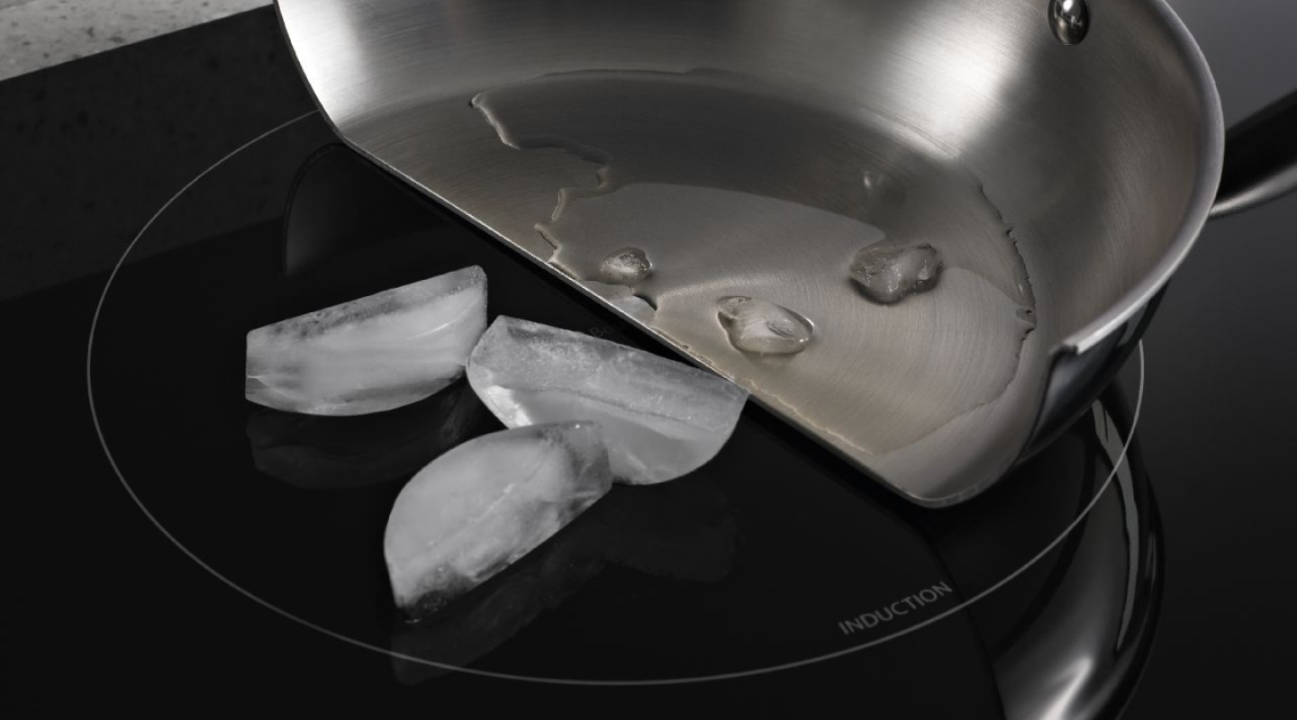 Pan cut in half with melted ice in the pan and whole ice cubes on the induction cooktop surface