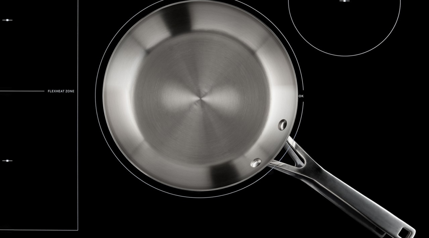 An empty, stainless steel pan on a glass cooktop surface