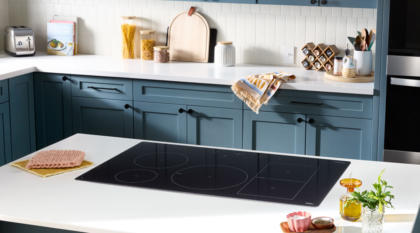 Black induction cooktop on a kitchen island in a kitchen with white countertops and teal cabinets