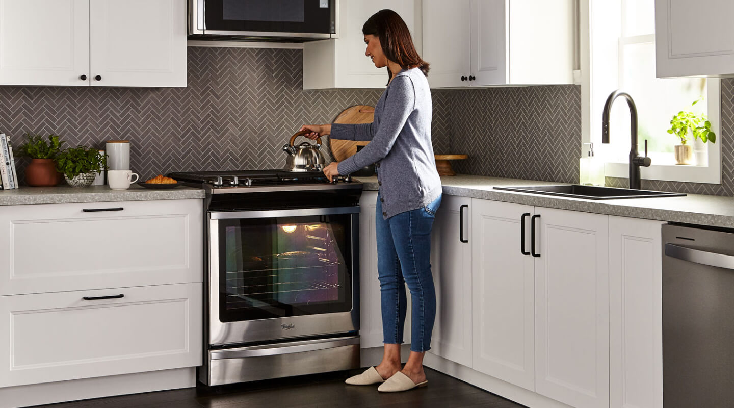 A person placing a tea kettle on the stovetop of a Whirlpool® gas oven in a modern kitchen. A person placing a tea kettle on the stovetop of a Whirlpool® gas oven in a modern kitchen.