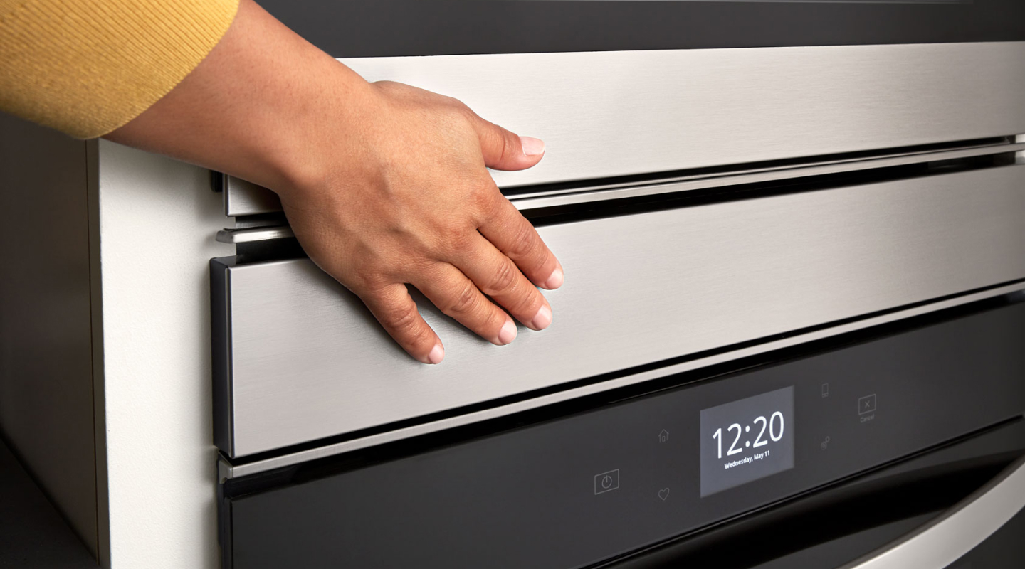 Person’s hand over an oven door above a digital display Person’s hand over an oven door above a digital display
