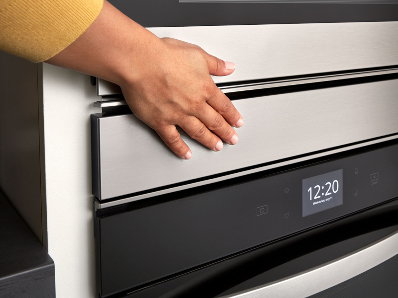 Person’s hand over an oven door above a digital display Person’s hand over an oven door above a digital display